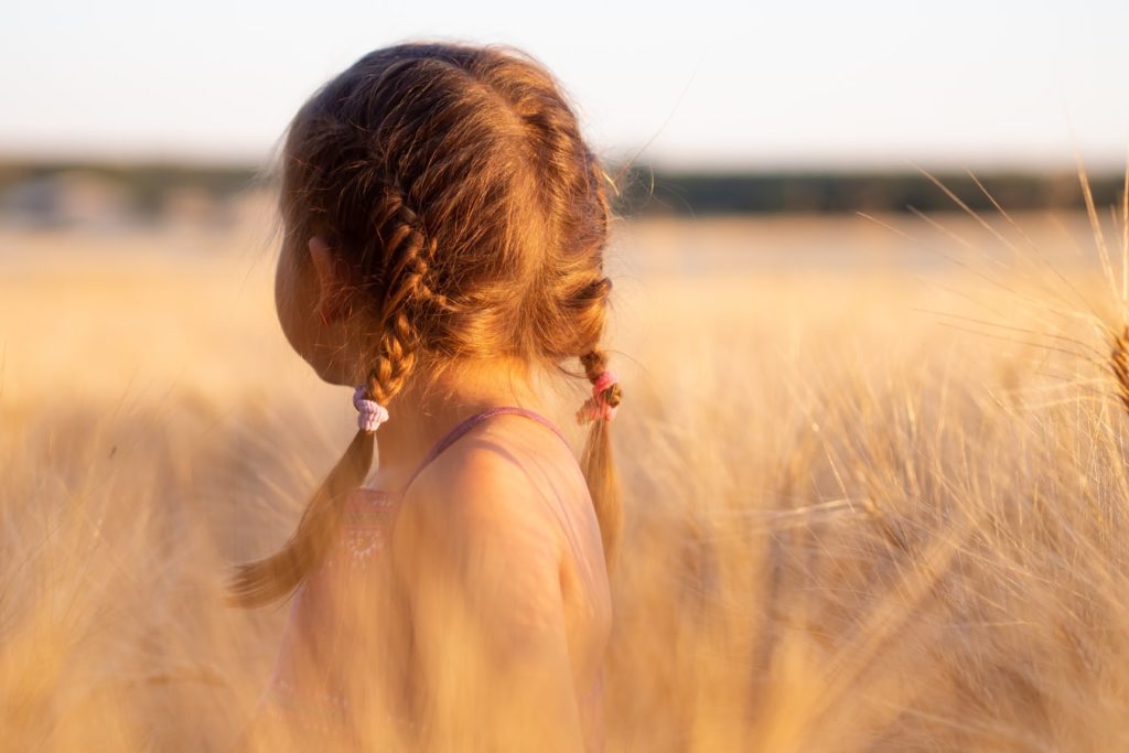 Fetiță care stă pe câmp și privește în depărtare