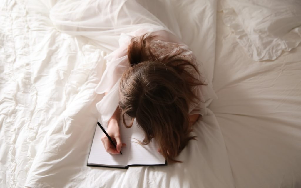 Femeie care stă în pat și scrie în jurnal