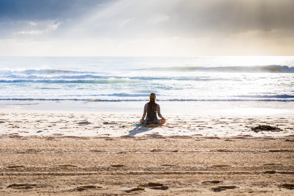 Femeie care stă pe plajă și meditează