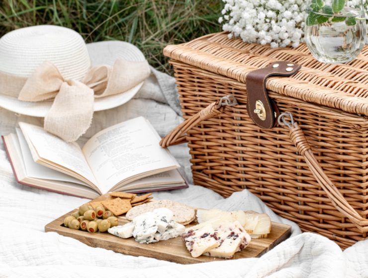Coș de picnic, platou cu brânzeturi, carte și o pălărie